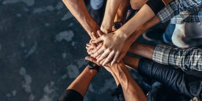 Top view of creative professionals putting their hands together as a symbol of teamwork, cooperation and unity. Stack of hands of men and woman.